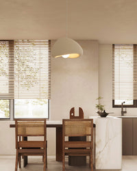 Cream eggshell pendant lighting above a wood dining table beside a marble kitchen island, paired with cane-back chairs in a warm neutral interior.