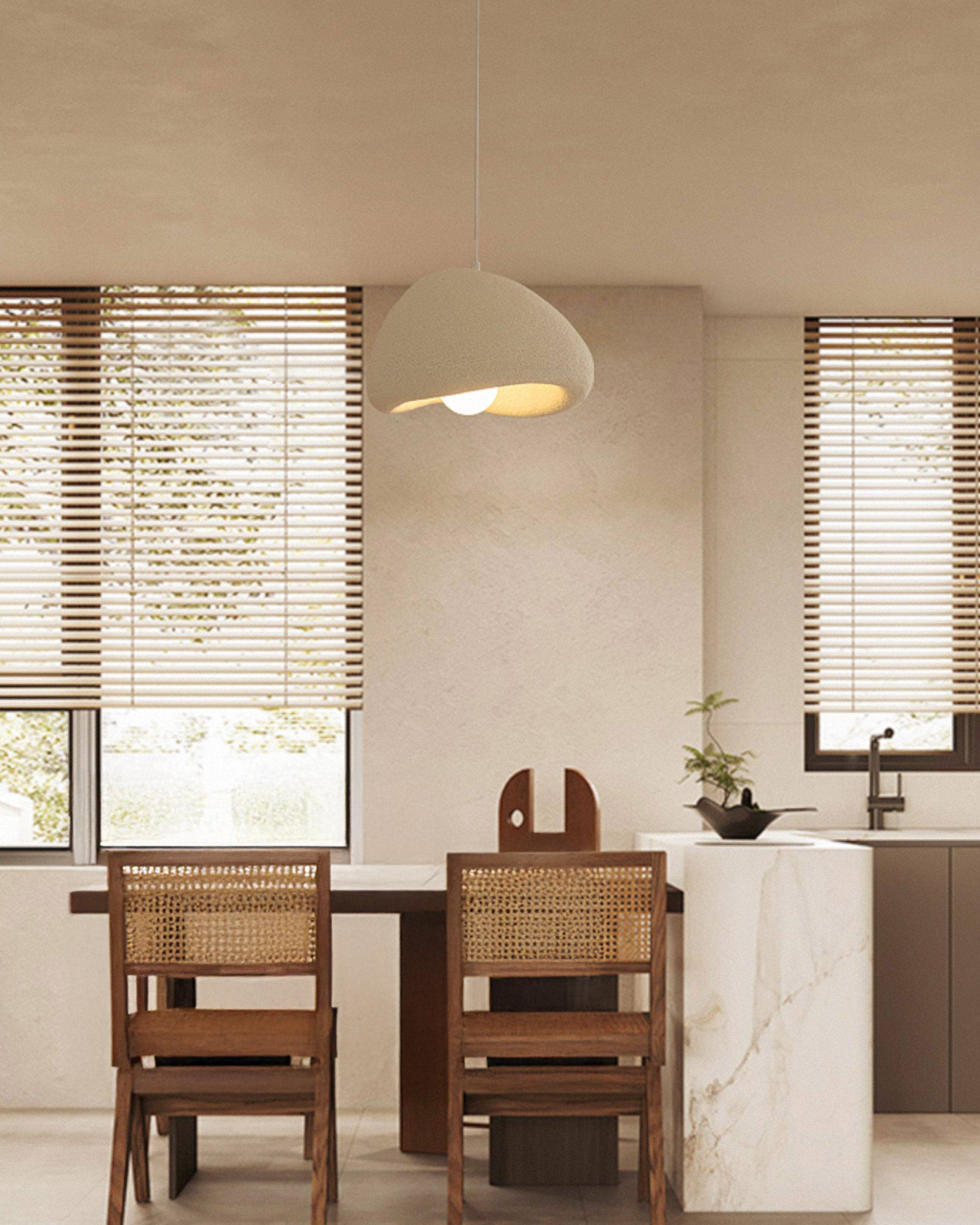 Cream eggshell pendant lighting above a wood dining table beside a marble kitchen island, paired with cane-back chairs in a warm neutral interior.