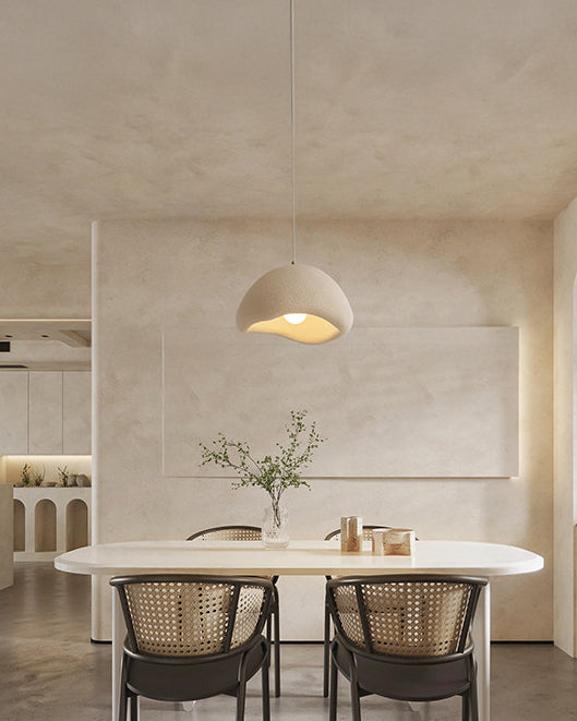Cream dome pendant light centered above an oval dining table in a softly textured neutral room with cane dining chairs.