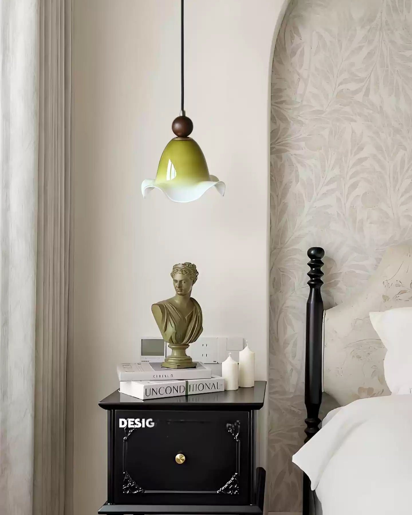 Olive glass hanging lamp glowing softly above a black bedside cabinet in a quiet bedroom with pale botanical wallpaper.