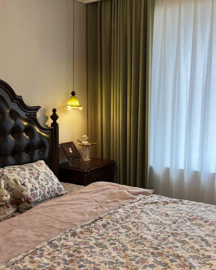 Olive vintage pendant lighting beside a dark upholstered bed, bringing a soft green glow and intimate warmth to the bedroom.