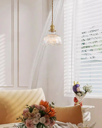 Sunlit sitting area with a ribbed glass pendant light above cream seating, flowers, and a side table.