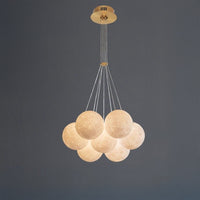 Full view of the seven-light bubble chandelier on a dark grey background, showing its compact globe cluster, slim cables and round gold-toned canopy.