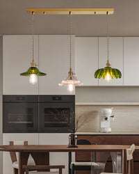 Linear chandelier with three mixed green and clear flower-shaped glass pendants above a wood dining table in an open kitchen and dining space.