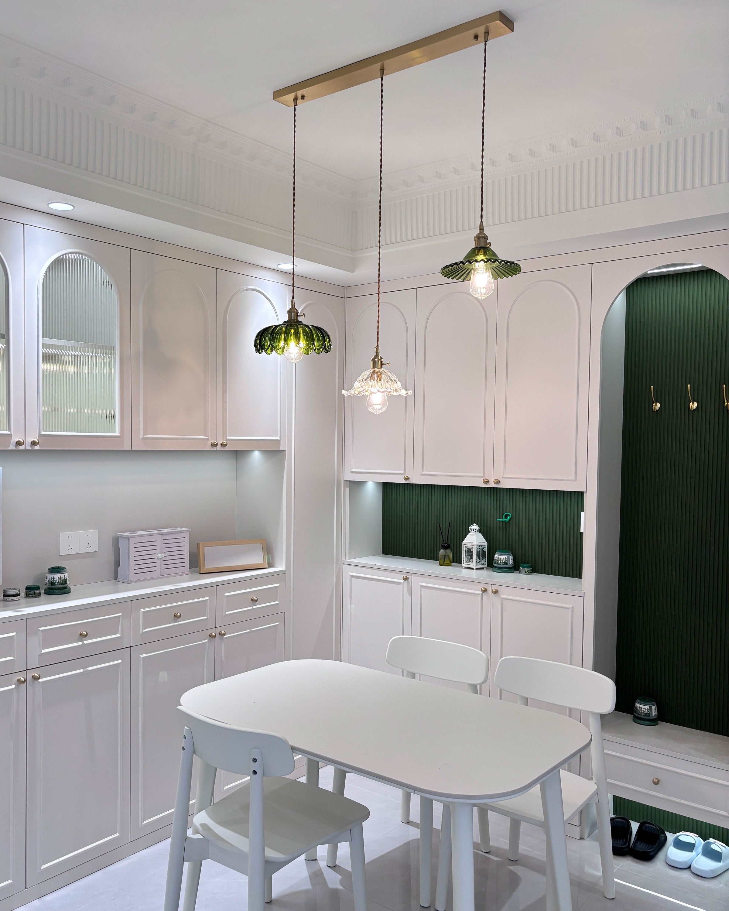 Bright white dining nook with a dining room chandelier featuring three mixed green and clear floral glass shades on a long metal canopy.