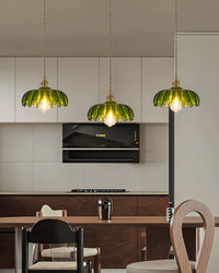 Kitchen close-up of a linear fixture where each green pendant light has a flower-shaped glass shade and glows above a wood table.
