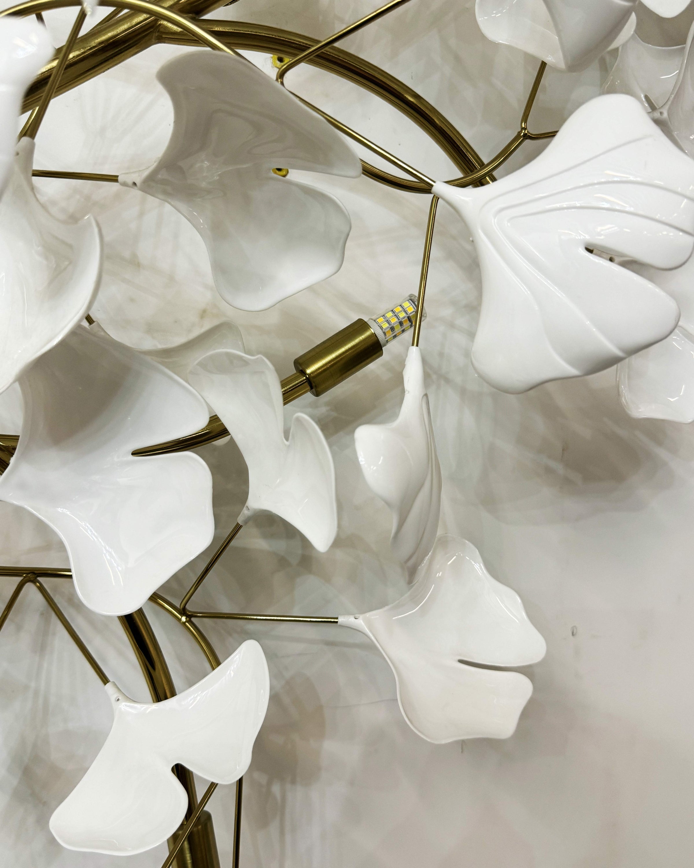 Close-up of glossy white ceramic ginkgo leaves, gold branches and an unlit replaceable LED bulb.