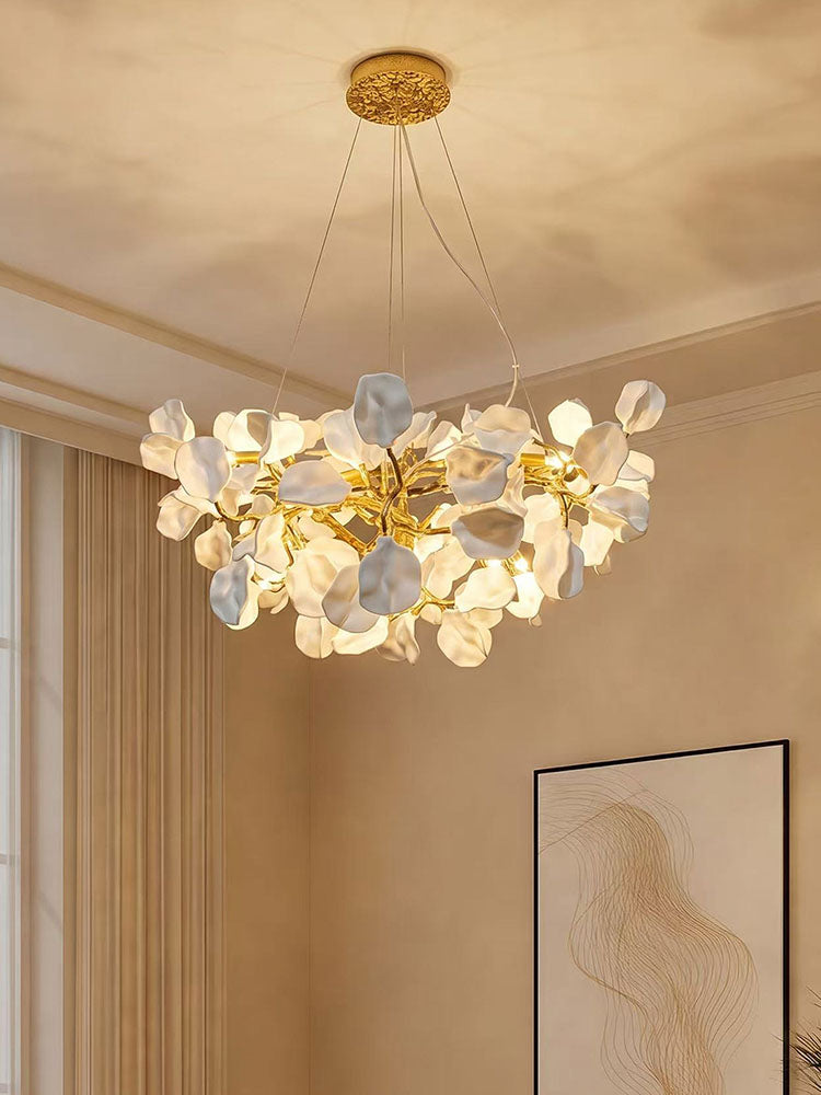 White ceramic flowers softly illuminated on a brass branching chandelier in a bright cream-toned room.