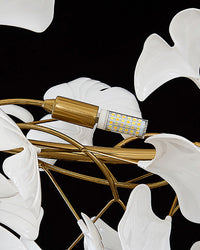 Close-up of the replaceable LED bulb set among white ceramic leaves on the gold frame.
