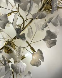 Close-up of the flush mount light with warm illumination behind white ceramic ginkgo leaves and gold branches.