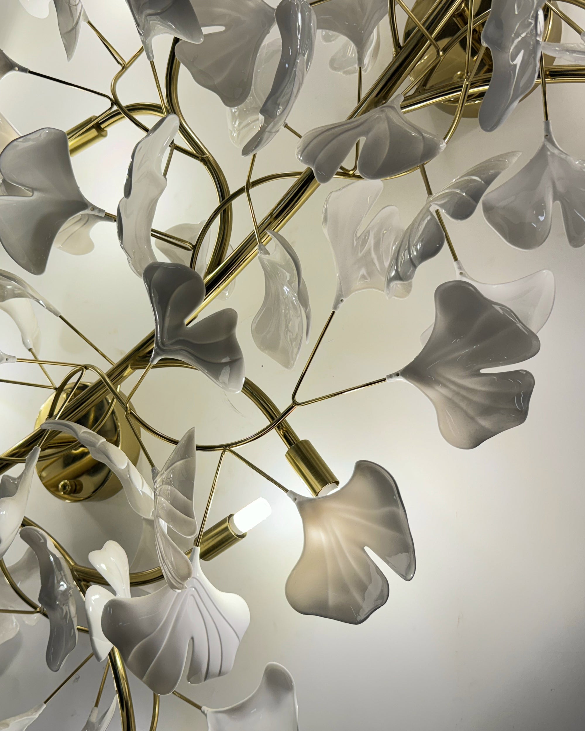 Close-up of the flush mount light with warm illumination behind white ceramic ginkgo leaves and gold branches.