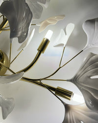 Close-up of included replaceable LED bulbs set between white ceramic ginkgo leaves and gold branches.