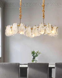Close view of a glass chandelier above a dining table, showing irregular white-swirled glass pieces layered across the softly undulating gold frame.