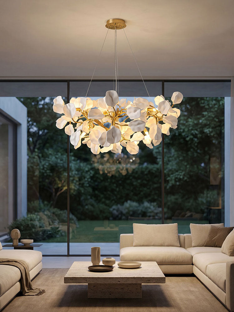 Round botanical chandelier casting layered warm light above a living room coffee table beside garden windows.