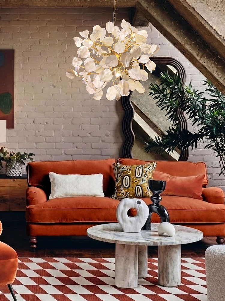 WOMO WM3353 living room chandelier with white ceramic petals and brass branches above an orange sofa in an eclectic lounge.