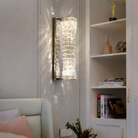 Chrome crystal wall sconce mounted beside a bed and built-in shelving, casting soft reflected light