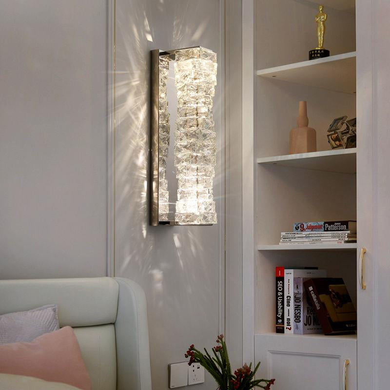 Chrome crystal wall sconce mounted beside a bed and built-in shelving, casting soft reflected light
