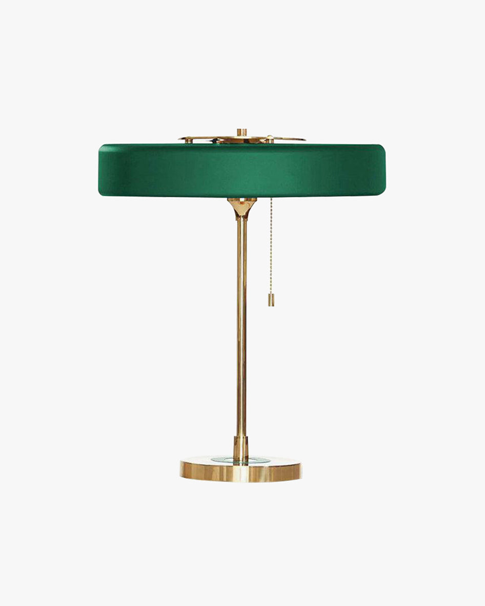 Green mid century table lamp with a wide round metal disc shade, slim gold-tone frame, circular base and hanging pull chain on white.