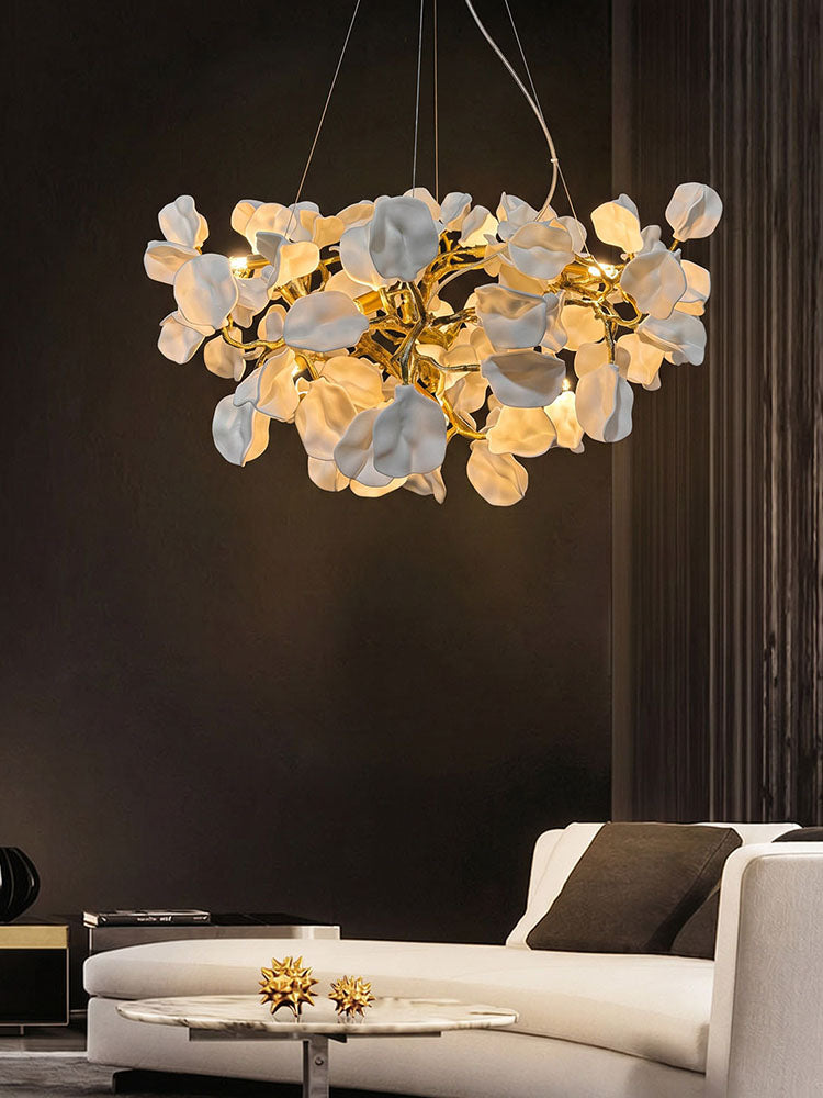 Sculptural chandelier of glowing ceramic flowers and brass branches above a white living room sofa.