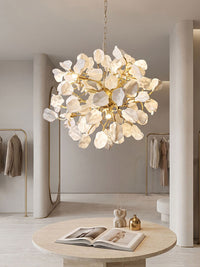 White ceramic pendant chandelier suspended by a brass chain above a round stone table in a calm neutral interior.