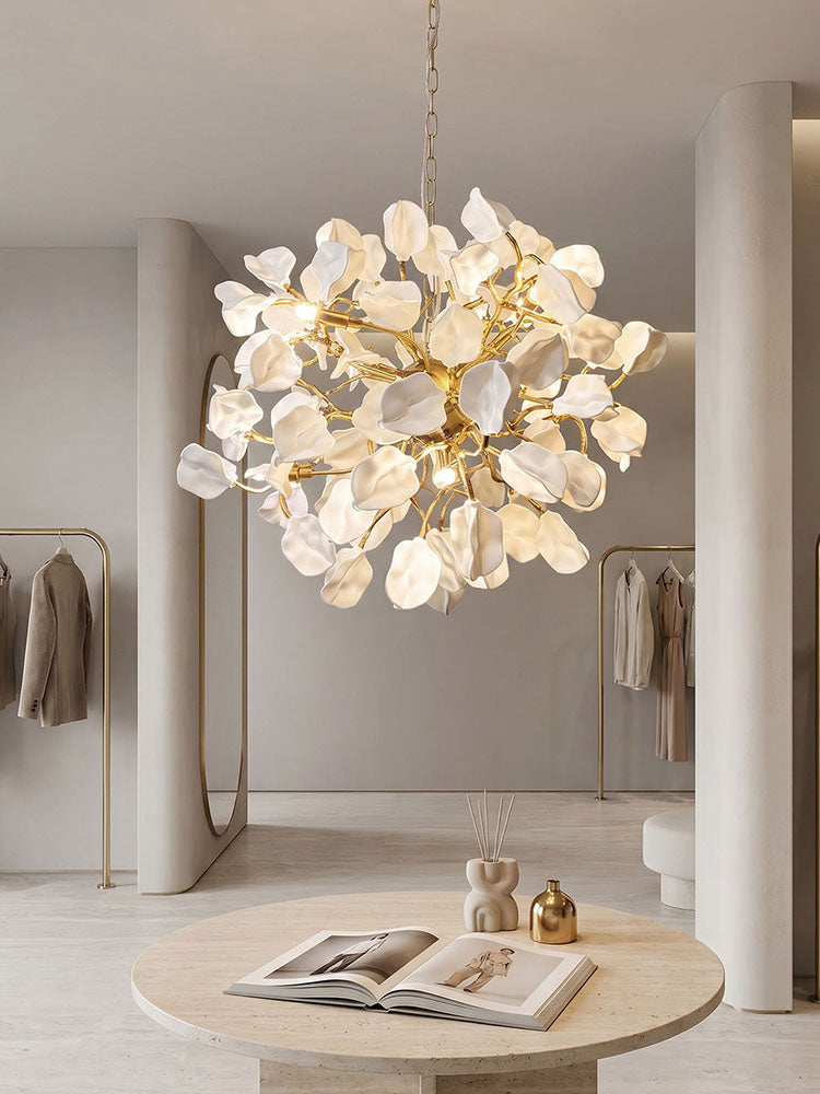 White ceramic pendant chandelier suspended by a brass chain above a round stone table in a calm neutral interior.