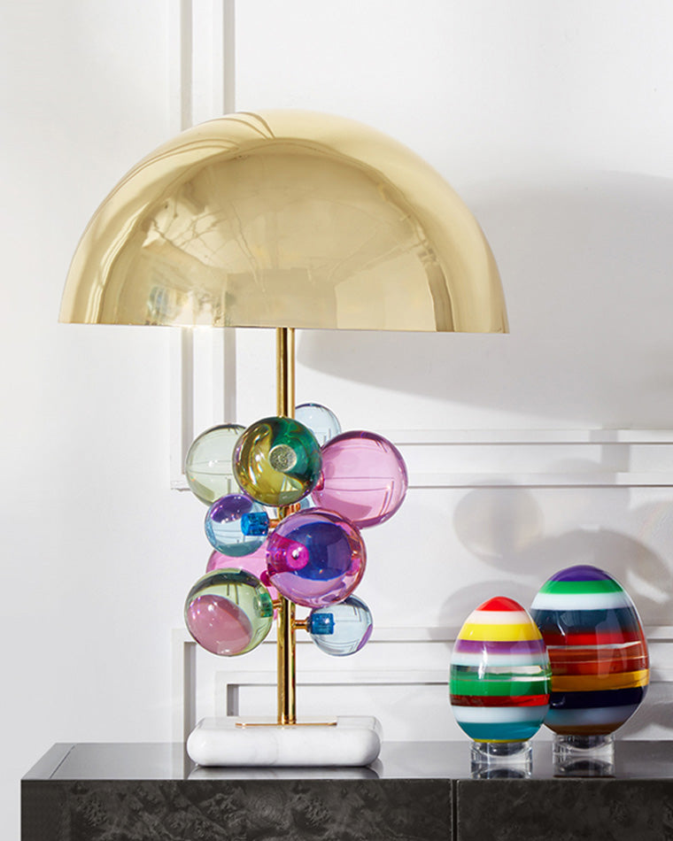 Colorful sculptural table lamp displayed on a black console beside two striped glass ornaments in a bright white interior.