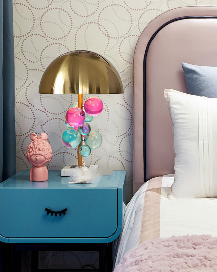 Colorful mushroom table lamp on a blue bedside cabinet in a pink bedroom with patterned wallpaper and white bedding.