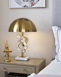Clear marble table lamp glowing on a neutral bedroom nightstand beside a gold rabbit figure and white bed.