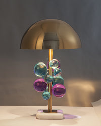 Lit modern mushroom lamp with pink, teal and clear acrylic orbs casting soft reflections on a gray wall.
