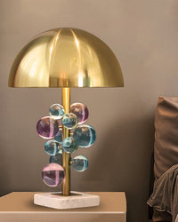 Illuminated mushroom lamp with jewel-toned acrylic spheres on a side table beside a brown upholstered seat.
