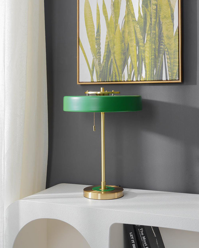 Green living room table lamp on a sculptural white console beneath botanical artwork against a charcoal wall.