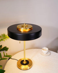 Illuminated black led table lamp viewed from above on a round covered table beside a teacup and leafy plant.