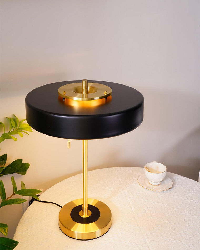Illuminated black led table lamp viewed from above on a round covered table beside a teacup and leafy plant.