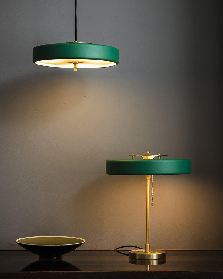 Green mid century modern lamp on a dark console beneath a matching suspended light, both casting warm downward illumination.