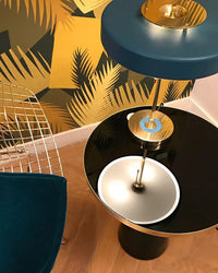 Blue metal table lamp viewed from above on a glossy black side table, showing the circular shade, gold-tone base and reflection.