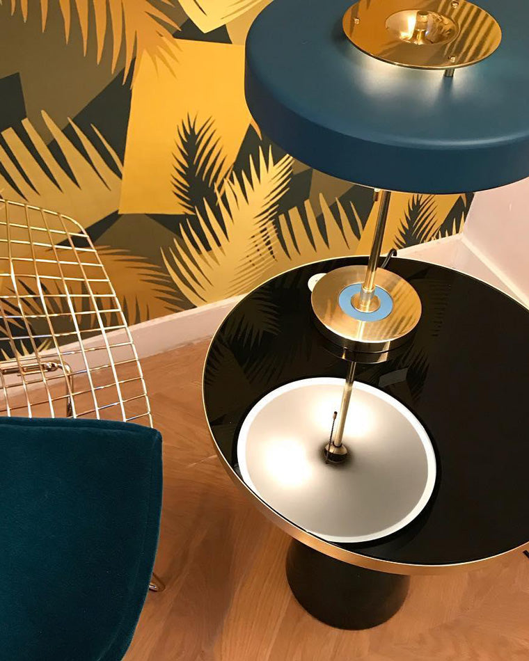 Blue metal table lamp viewed from above on a glossy black side table, showing the circular shade, gold-tone base and reflection.