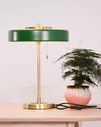Green pull chain table lamp beside a potted plant, showing the round gold-tone base, hanging chain, cord and inline switch.