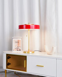 Red modern table lamp glowing on a white fluted console with gold accents, framed books and a curved white sculpture.