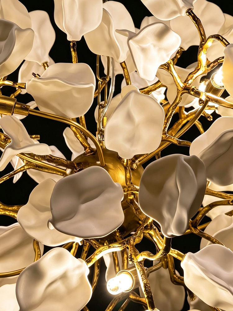 Close-up of the ceramic chandelier, showing sculpted white leaf-and-petal forms, golden brass branches, clear wiring and visible G9 LED bulbs.