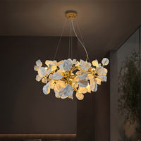 Modern flower chandelier with glowing white ceramic blooms and brass branches in a dark living room.