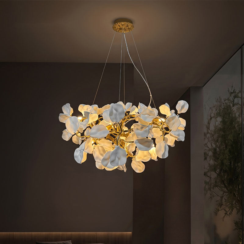 Modern flower chandelier with glowing white ceramic blooms and brass branches in a dark living room.