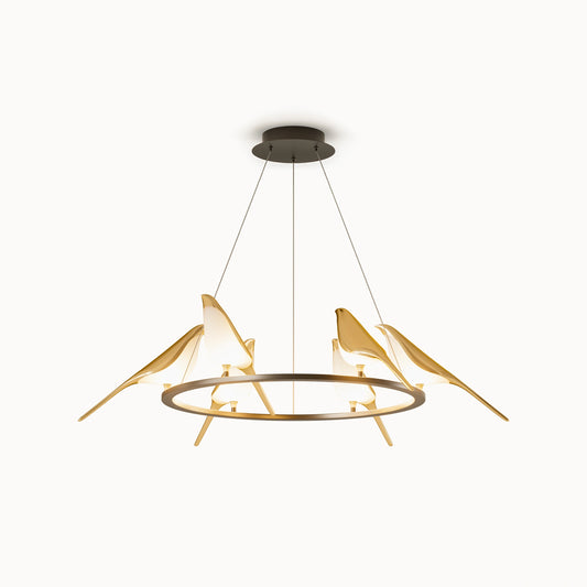 Angled view of the gold bird ceiling light, showing illuminated acrylic bird bodies, long gold tails, suspension cables, and the round canopy.