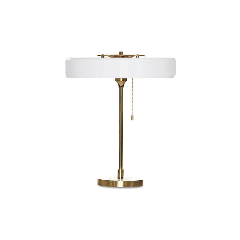 White led table lamp with a wide circular metal shade, gold-tone frame, round base and hanging pull chain.