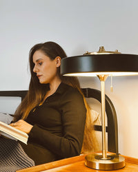 Black pull chain lamp casting warm downward light beside a woman reading in bed.