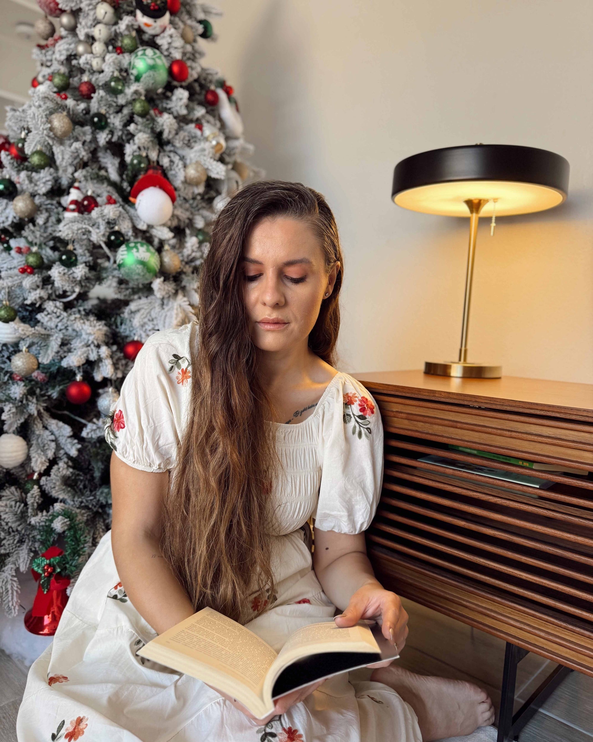 Black vintage table lamp glowing on a wooden console beside a decorated Christmas tree and a reading chair.