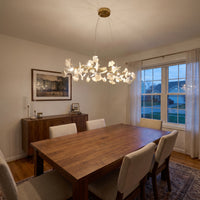 Warm-lit gold ginkgo leaf chandelier above a rectangular dining table at dusk.