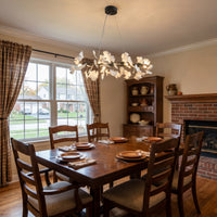 Ceramic ginkgo leaf linear chandelier above a long wooden table in a bright casual dining room.