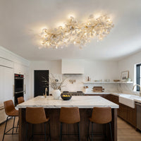 Long ceramic flush mount light with white ginkgo leaves and gold branches above a marble kitchen island.