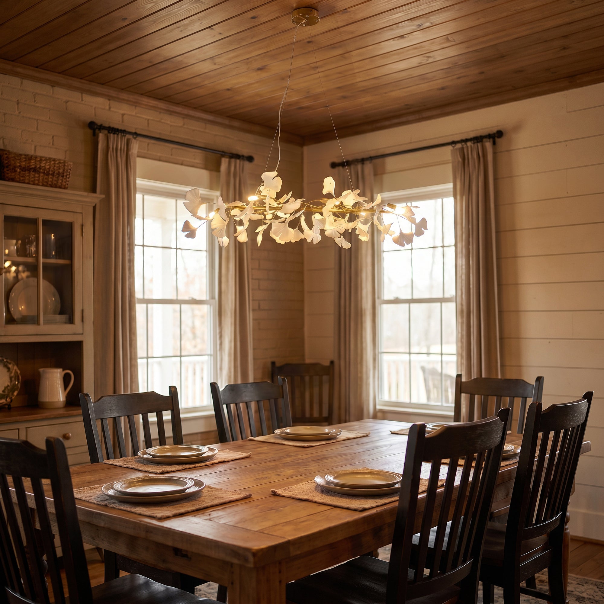Gold ginkgo leaf chandelier lighting a rustic wooden dining table in a warm, wood-paneled room.