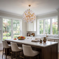 An elegant bright kitchen with a dark wood island and white marble countertop; a large white and gold chandelier with petal-like shades hangs above the island.